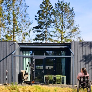 Im Vordergrund ist Kim ihrem Rollstuhl Lutzi im Garten vor der Terrasse unser rollstuhlgerechten Ferienlodge im Park Zeegser Duinen in der Niederlande