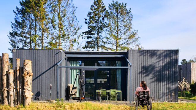 Im Vordergrund ist Kim ihrem Rollstuhl Lutzi im Garten vor der Terrasse unser rollstuhlgerechten Ferienlodge im Park Zeegser Duinen in der Niederlande